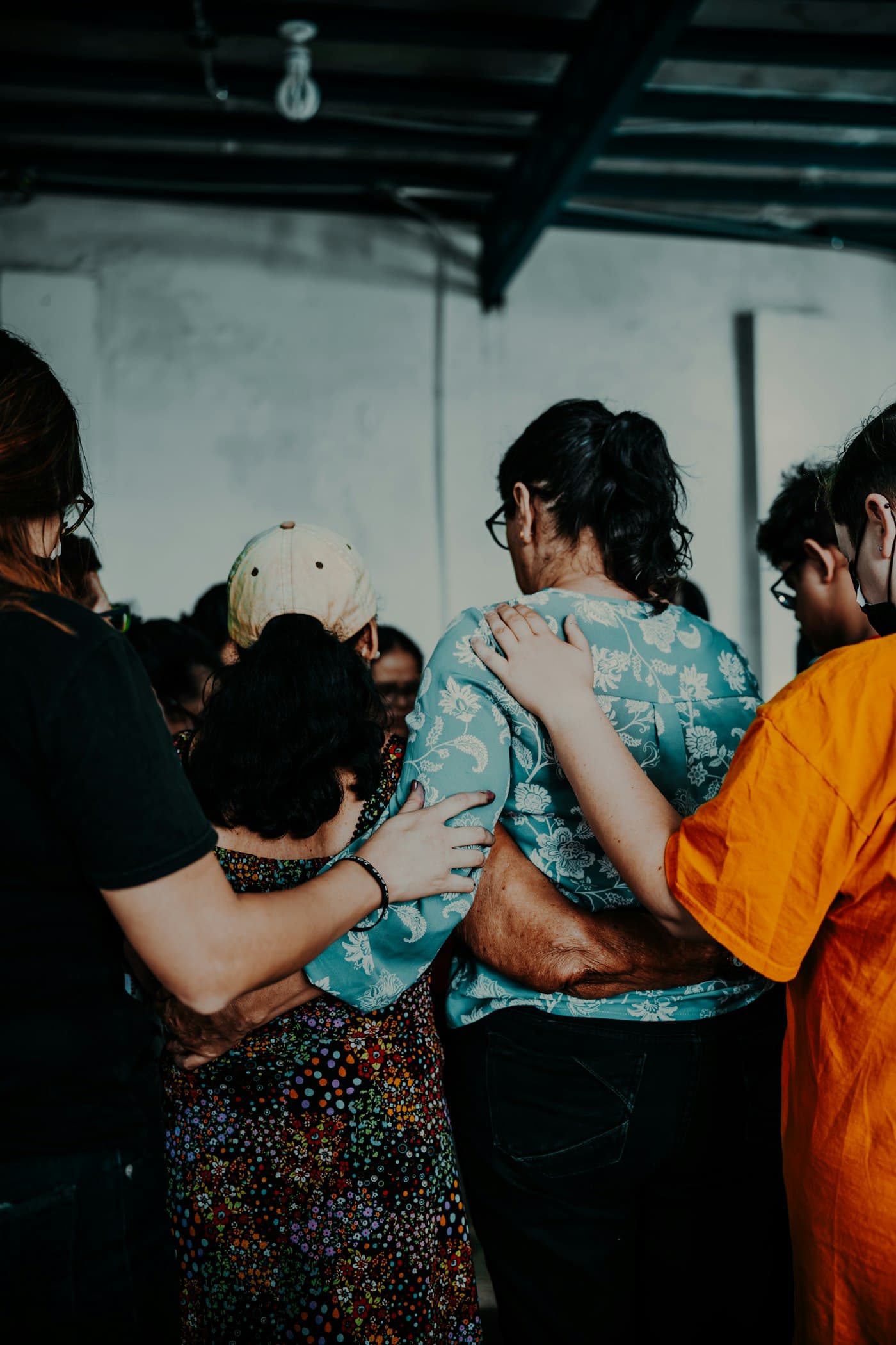 A multicultural group of friends standing in a circle, arms around each other in support